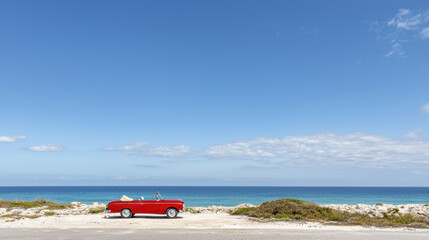Fototapeta premium vibrant red convertible parked by serene ocean under clear blue sky