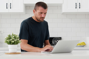 Man sits at modern kitchen using laptop.