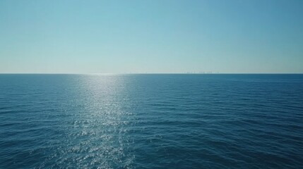 Fototapeta premium Calm Ocean Waters with Distant Wind Farm on Horizon on Sunny Day