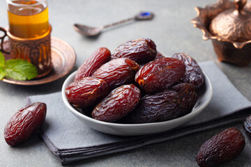 Fresh Medjool Dates in a bowl with tea. Ramadan Kareem. Grey stone background. Close up.