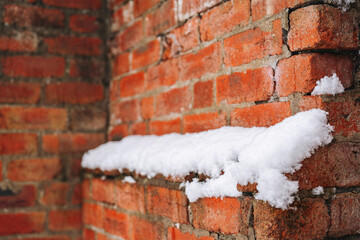 Snow covers a rustic brick wall in a quiet, winter setting, showcasing the beauty of seasonal...