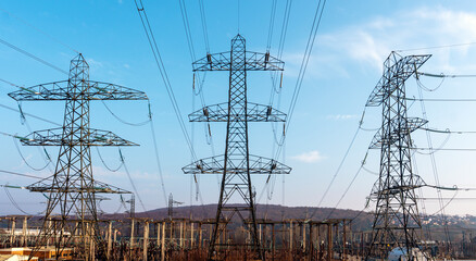 High voltage power lines stretch across the landscape under a clear blue sky, showcasing the...