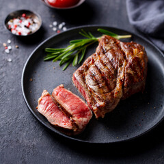 Beef Steak medium rare on a black plate. Dark grey background. Close up.