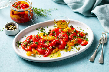 Marinated yellow and red bell pepper salad with capers and olive oil. Blue background. Close up.