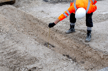 Construction worker measuring trench depth on site
