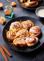 Cinnamon rolls, cinnabons on black plate. Grey background. Close up.