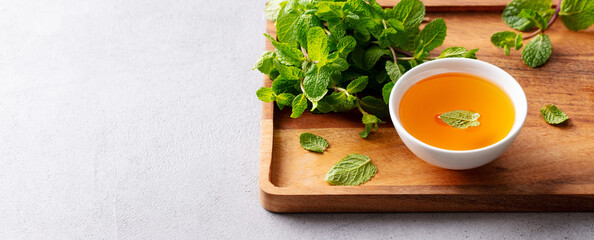 Fresh tea with mint in a bowl on a wooden tray. Grey background. Close up. Copy space.