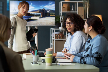 Female team sitting at table and discussing new project at meeting