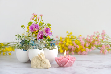 decorative Easter bunny, floral candle, colorful flowers in egg shells close up on light background. Easter or Ostara holidays concept. festive composition for spring season