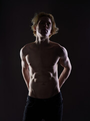 A young man with a bare torso, backlit to highlight his sculpted muscles and silhouette. The athletic physique and fitness training create a powerful image of a muscular body.