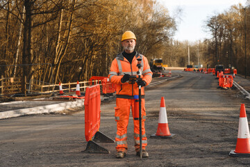 Worker wearing protective gear surveys a construction site with traffic cones and barriers...