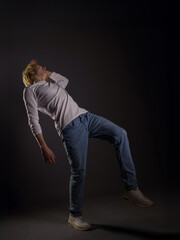Portrait of a young man with wavy blonde hair in white clothing against a dark background. His expression is serious, and his gaze is intense. Atmospheric lighting highlights facial features and hair 