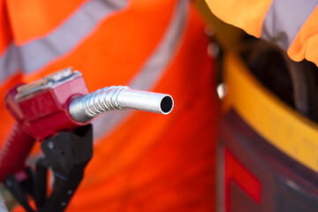 Fuel nozzle held by a worker in reflective safety vest while dispensing fuel at construction site gas station 