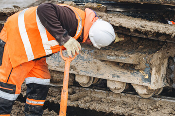 Construction worker inspects machinery while clearing tracks from mud 