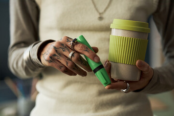 Close-up of businesswoman holding coffee drink and highlighter while working in office