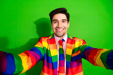 Charismatic young man wearing a colorful rainbow-striped suit with a green background, expressing...