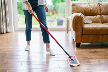 Fototapeta premium Person cleaning wooden floor in a bright living room with a casual atmosphere during daytime while wearing comfortable clothing and socks