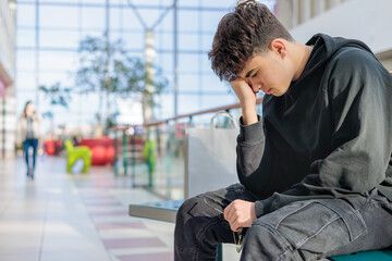 eenager in black hoodie sitting on a bench with head in hands, feeling stressed or overwhelmed,...