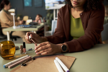 Close-up of businesswoman sitting at table in office and using varnish to make manicure