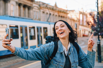 Young woman enthusiastically takes a selfie in a vibrant city during daylight, capturing the energy...