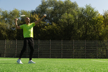 Strong caucasian badminton player racquet hit shuttlecock while practice before competition. Summer sports game, outdoors. Game moment.