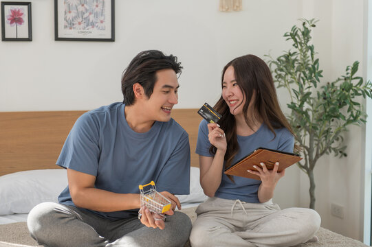 Young Asian couple shopping online while using digital tablet at home, Couple using credit card to pay bills or to book a room for vacation, making an online purchase - Powered by Adobe