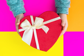 Baby hands with heart shaped gift box on a multicolored background