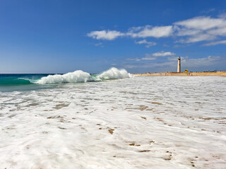 rough ocean waves in Fuerteventura, view of the lighthouse in Morro Jable