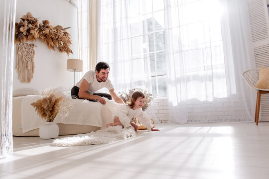 Father and daughter are enjoying a playful moment together, pulling a blanket on the bed in a brightly lit, cozy bedroom, creating a heartwarming scene of family bonding - Powered by Adobe