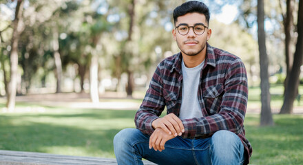 Hispanic young adult male in park wearing glasses and plaid shirt