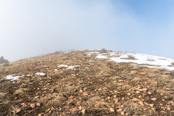 Winter hilltop of the Chatkal Mountain Range in Uzbekistan surrounded by clouds and lit by diffused sunlight.