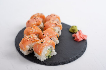 Fresh salmon sushi Philadelphia rolls with avocado and cream cheese, topped with sesame seeds, served on a black slate plate with wasabi and pickled ginger.