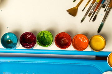 Vibrant art setup with colorful paint cans in blue, red, green, orange, and gold, alongside various brushes on a white surface. Perfect for creative projects and craft inspiration.
