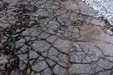 Cracked, dry asphalt surface with deep fissures and gravel on the side, showcasing natural textures. Ideal for construction, road repair, and environmental background concepts.