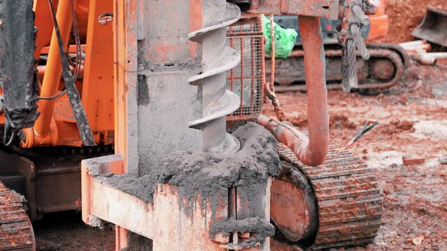 Piling rig drills deep into ground on site rotating auger axtracting soil