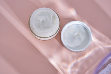 An open jar of cream with its texture on a pink background.