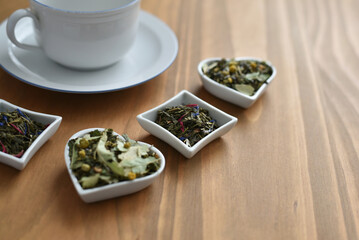 Tea cup and different teas in little bowls on wooden table