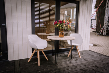 Two wooden chairs and a matching table are placed on the terrace of a charming white wooden house....