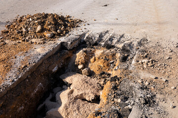 A sunny road construction site features a deep trench and scattered debris