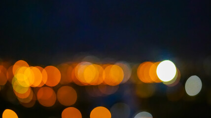 Defocused city lights at night creating bokeh effect. Abstract blurred background with glowing orange, yellow, and white circles. Nighttime urban illumination concept for design and print