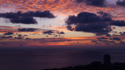 Dramatic sunrise over the sea with dark clouds and city skyline. Scenic seascape with colorful sky and cloud formations at twilight.
