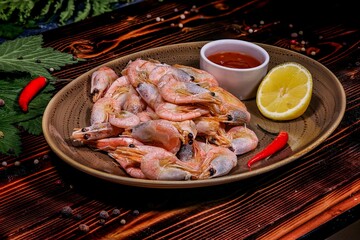 Delicious Boiled Shrimp with Sauce and Lemon on Plate, Chili Pepper Garnish, Dark Wooden Table with Greens.