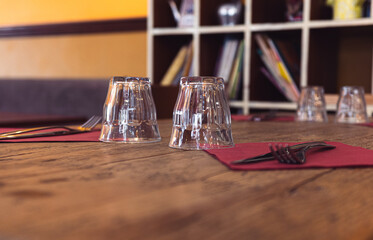 Two glasses and forks sit on red napkins on a wooden table. Restaurant setting, indoor scene