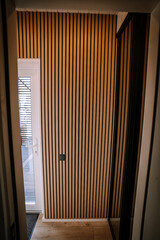 A modern interior with a stylish wooden slat wall, a glass door leading outside, and a mirrored wardrobe reflecting the space..