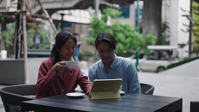 Asian b&uacute;shines copule analyzing information on tablet at outdoor cafe