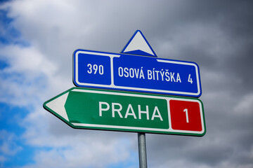 Directional road sign reading 'Praha on Highway D1' with clouds in the background.