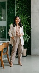 A Filipina professional woman in a white blazer over a neutral-toned pantsuit, posing in front of a nature-inspired office space.