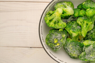 Frozen green broccoli in a ceramic bowl on a wooden table, close-up, top view.
