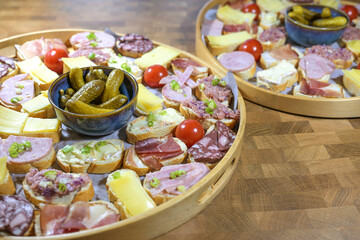 Party canapes, small sandwiches topped with cheese, ham and sausage on a round tray with a bowl of gherkins, simple finger food snack, selected focus
