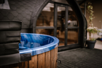 A close-up of a wooden hot tub with a blue interior, placed on a black deck near a modern black...